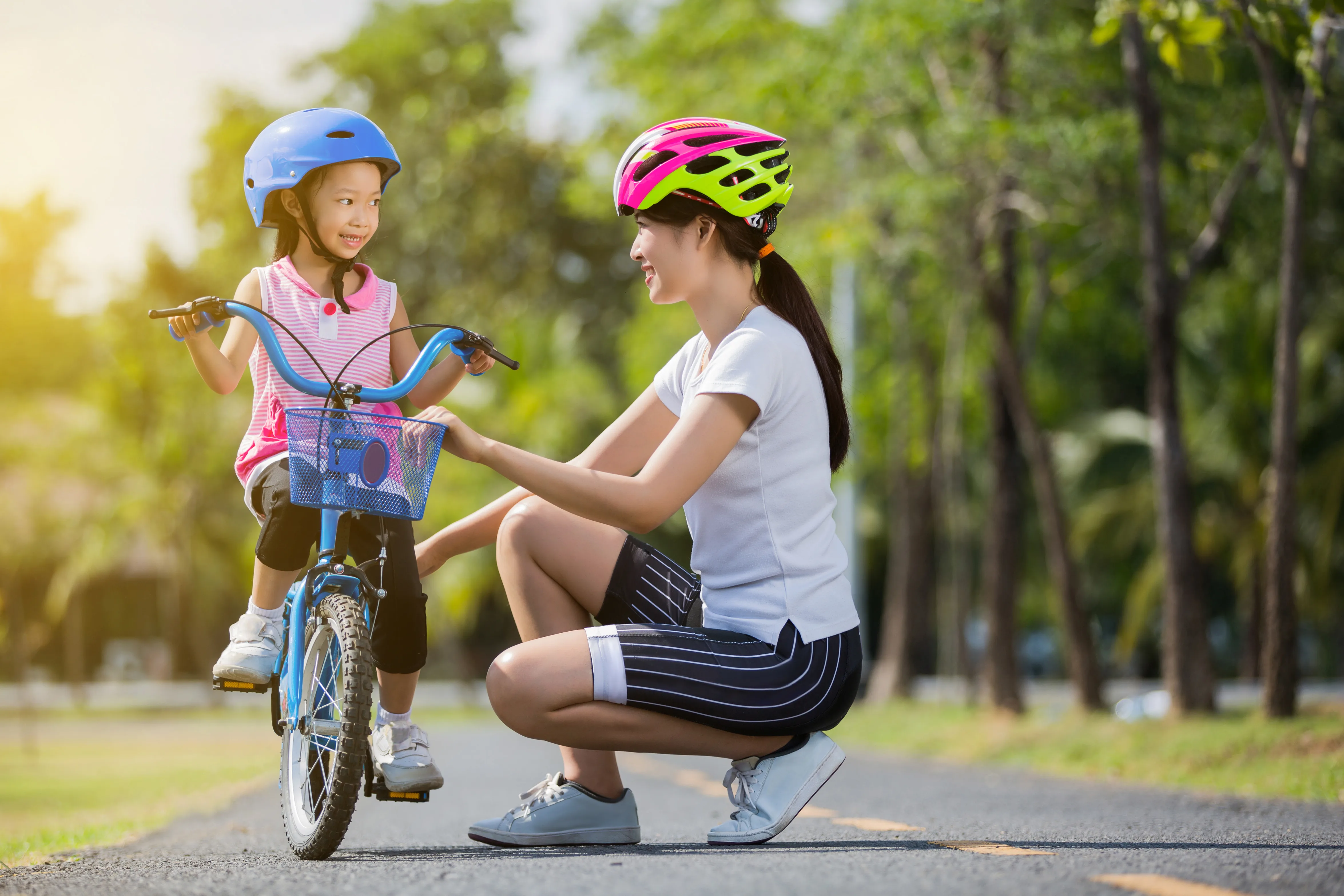 Two girls in cycling helmets beside a bicycle on a park path