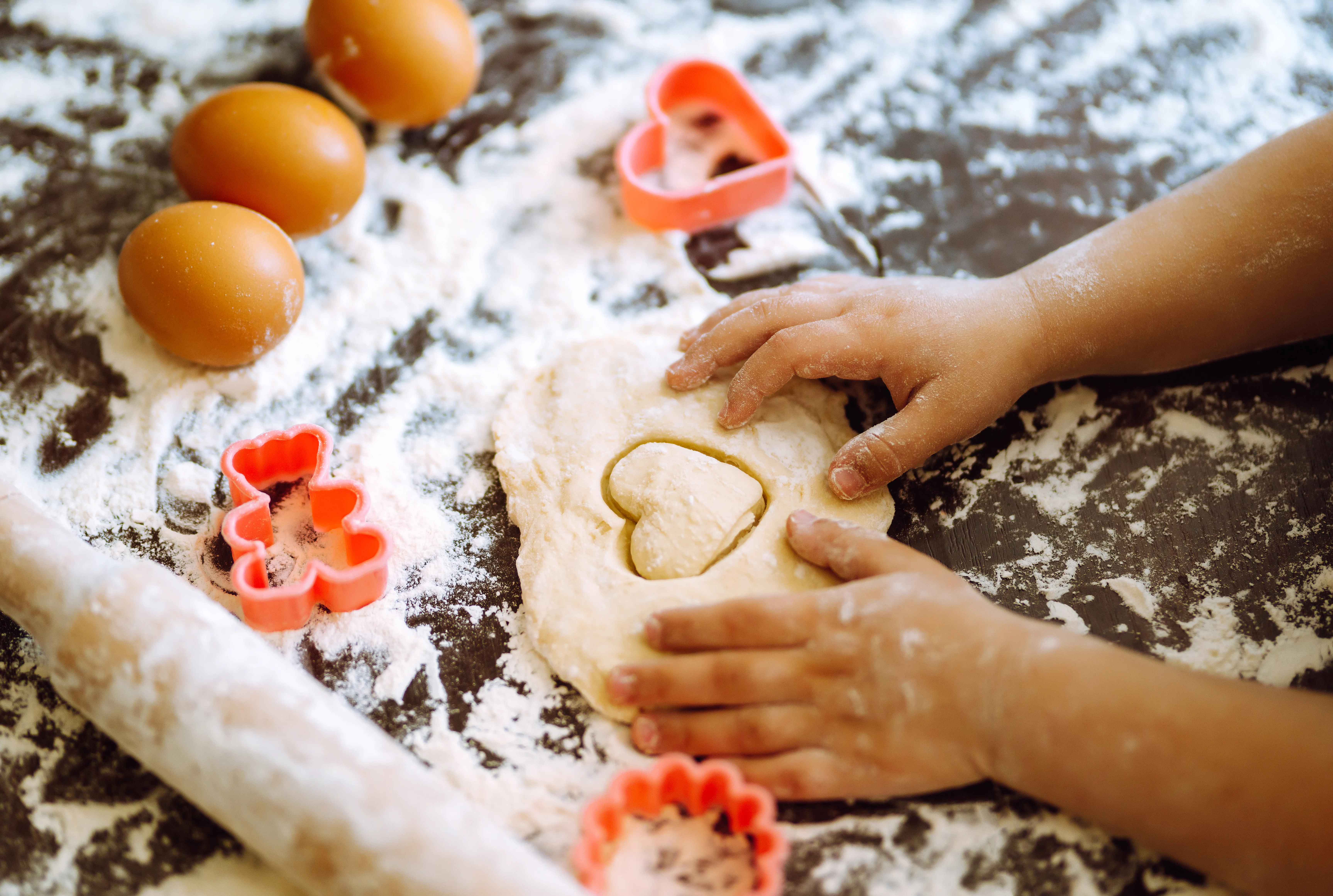 A child's hands cutting heart shapes out of dough with a cookie cutter