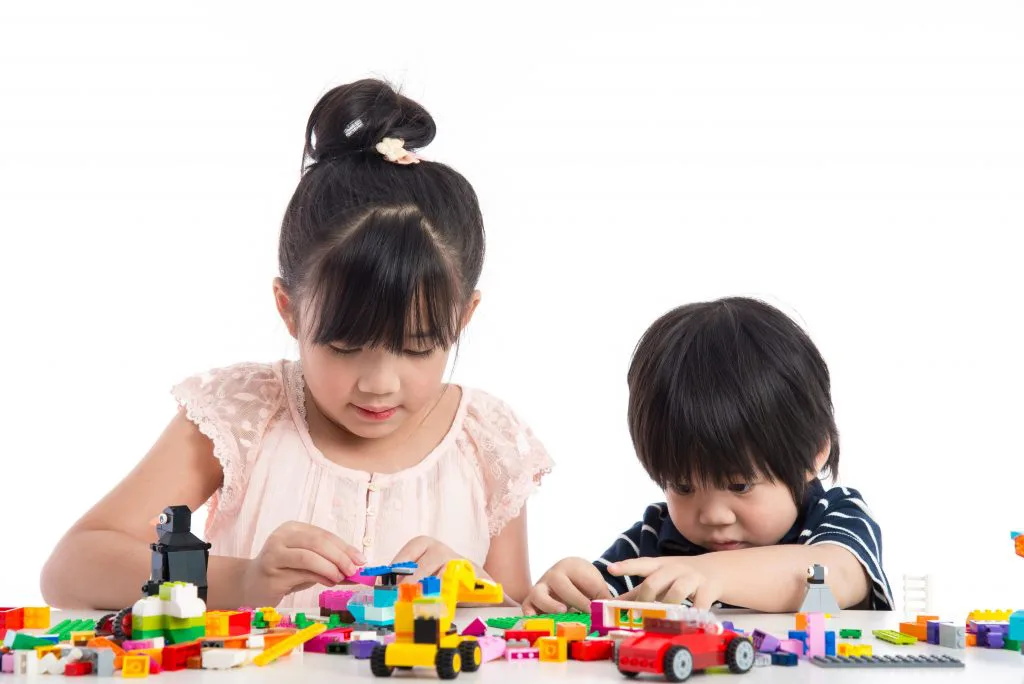 Two young children playing with coloured building blocks at a table