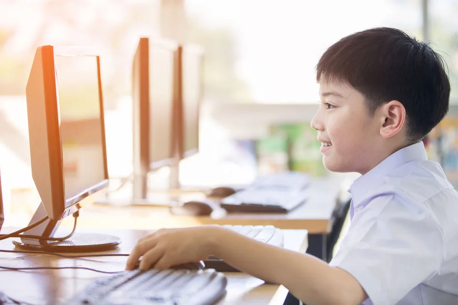 A boy typing at a desktop computer in a computer lab