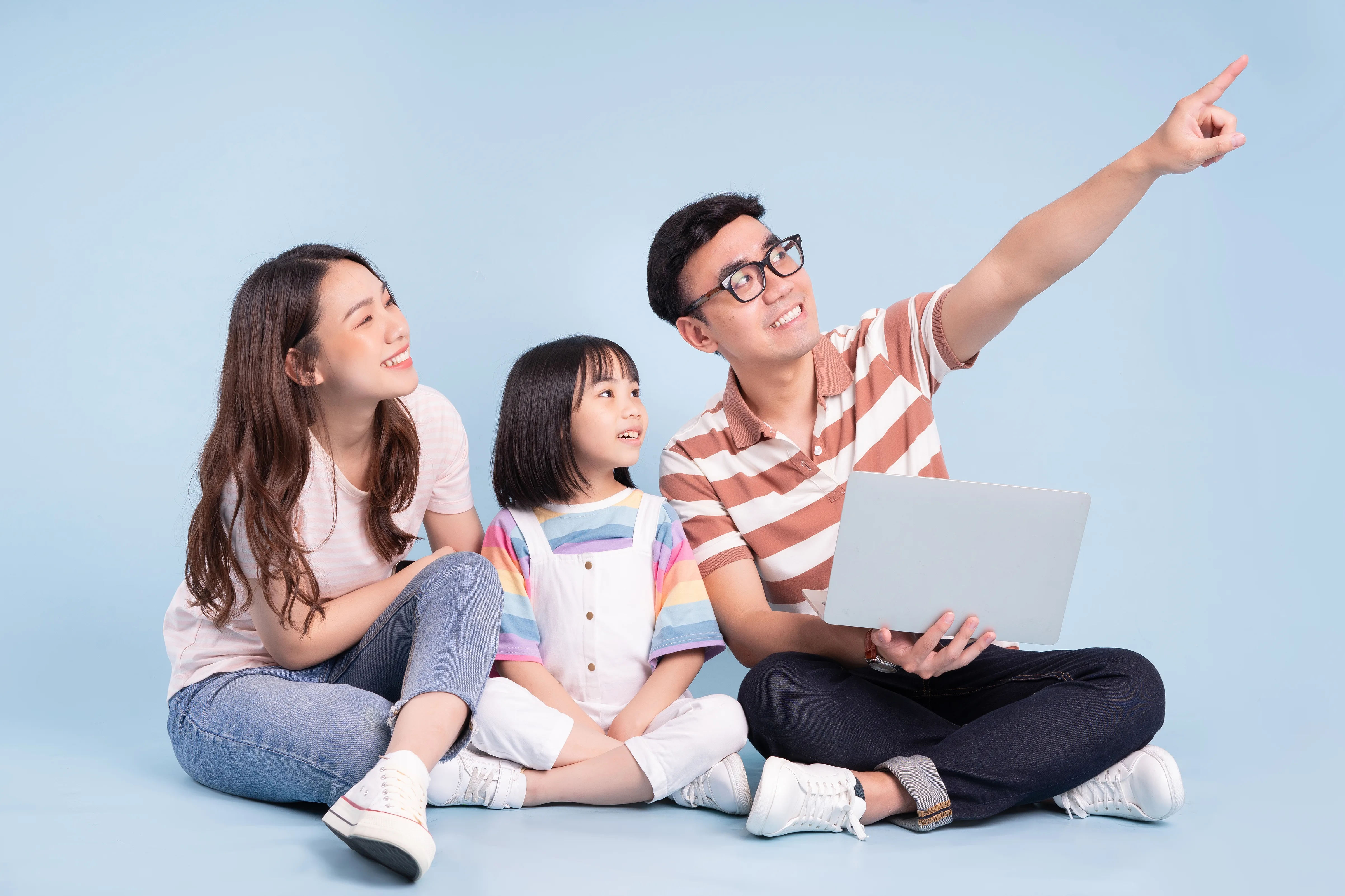 Parents and a young child sitting together with a laptop, the father pointing ahead
