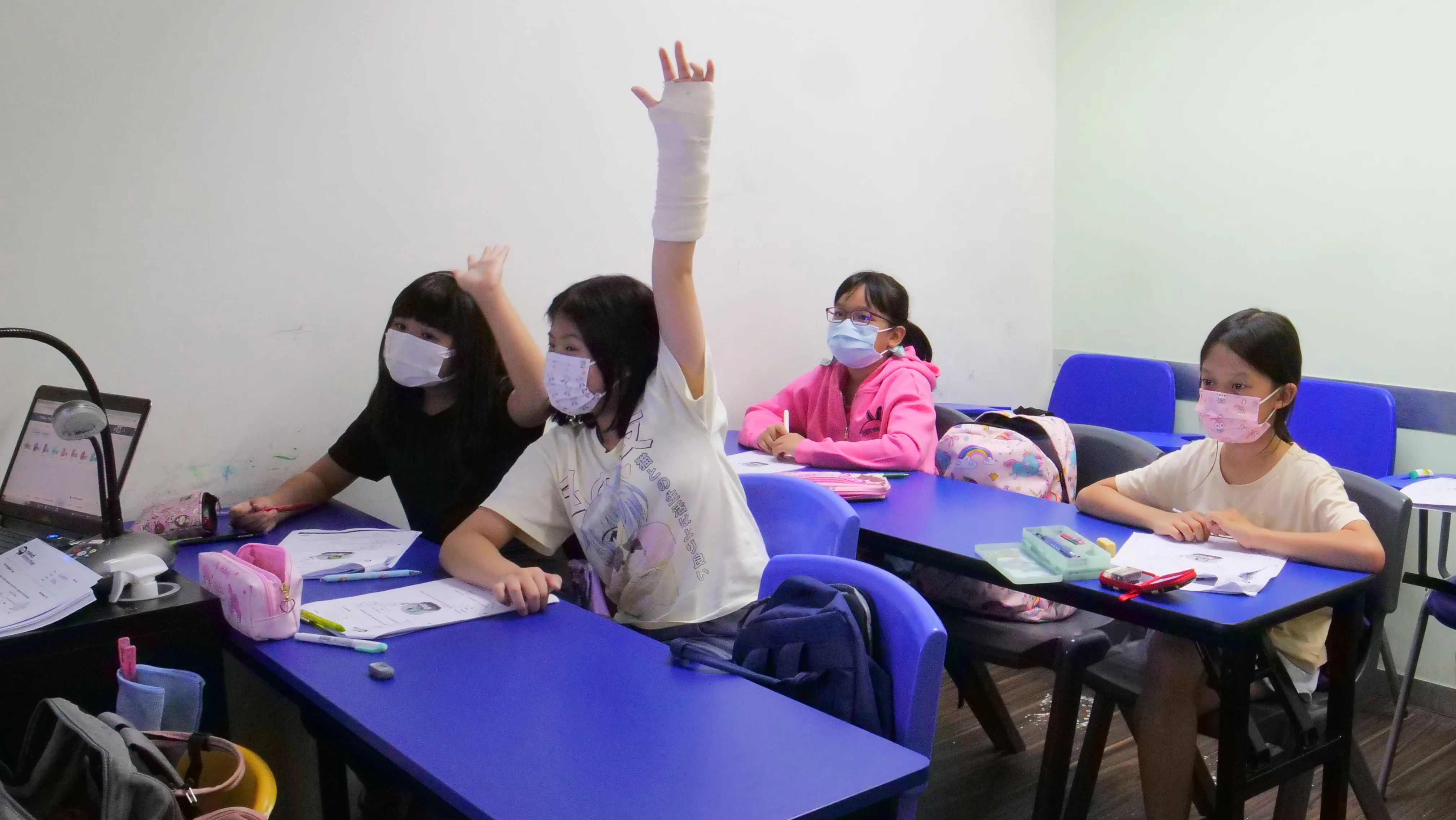 Children at desks in a Mind Stretcher classroom, one raising a hand