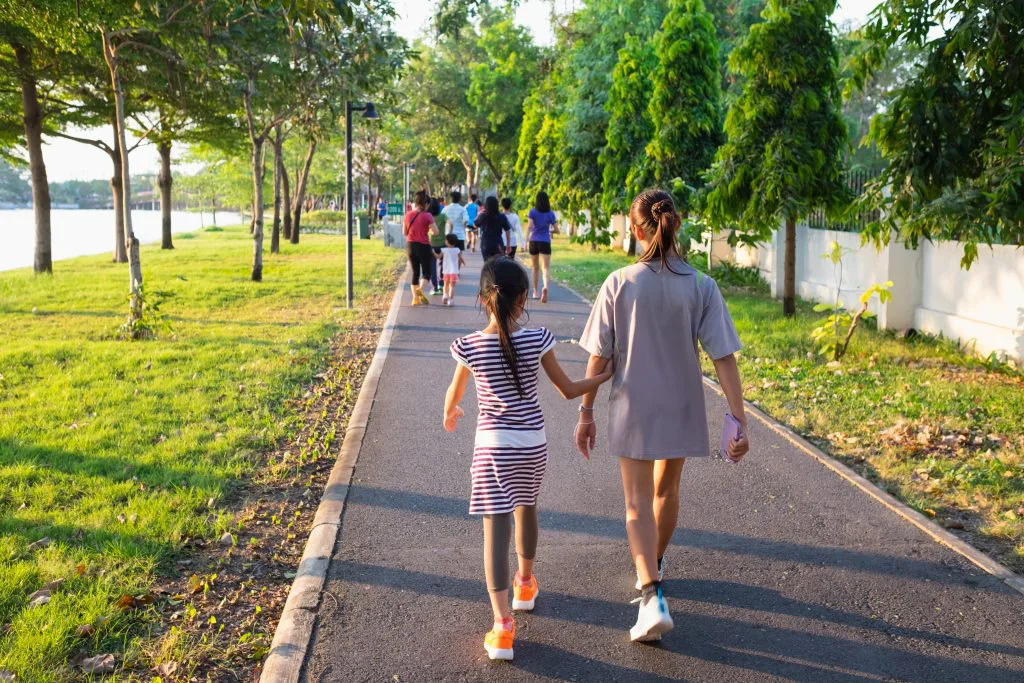 Two girls walking together along a tree-lined park path